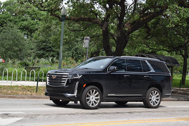 Houston, TX USA - 4-18-2025 - A portrait of a Cadillac Escalade luxury SUV with illuminated headlights on while cruising in a downtown district