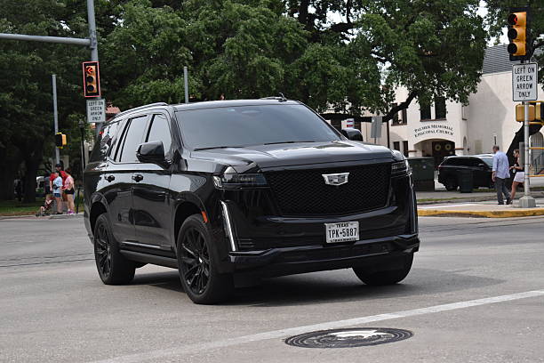 Houston, TX USA - 4-18-2025 - A portrait of a black Cadillac Escalade EV Sport luxury SUV cruising during rush hour in a downtown financial district near a residential area.